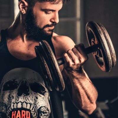 Bearded man in gym lifting a heavy dumbbell, showcasing strength and fitness.