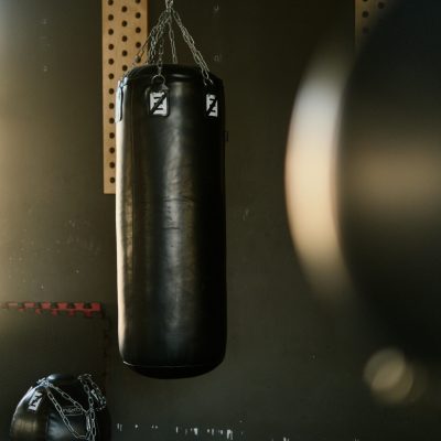 Black punching bag hangs in a gym, bathed in sunlight, creating a moody and focused atmosphere.